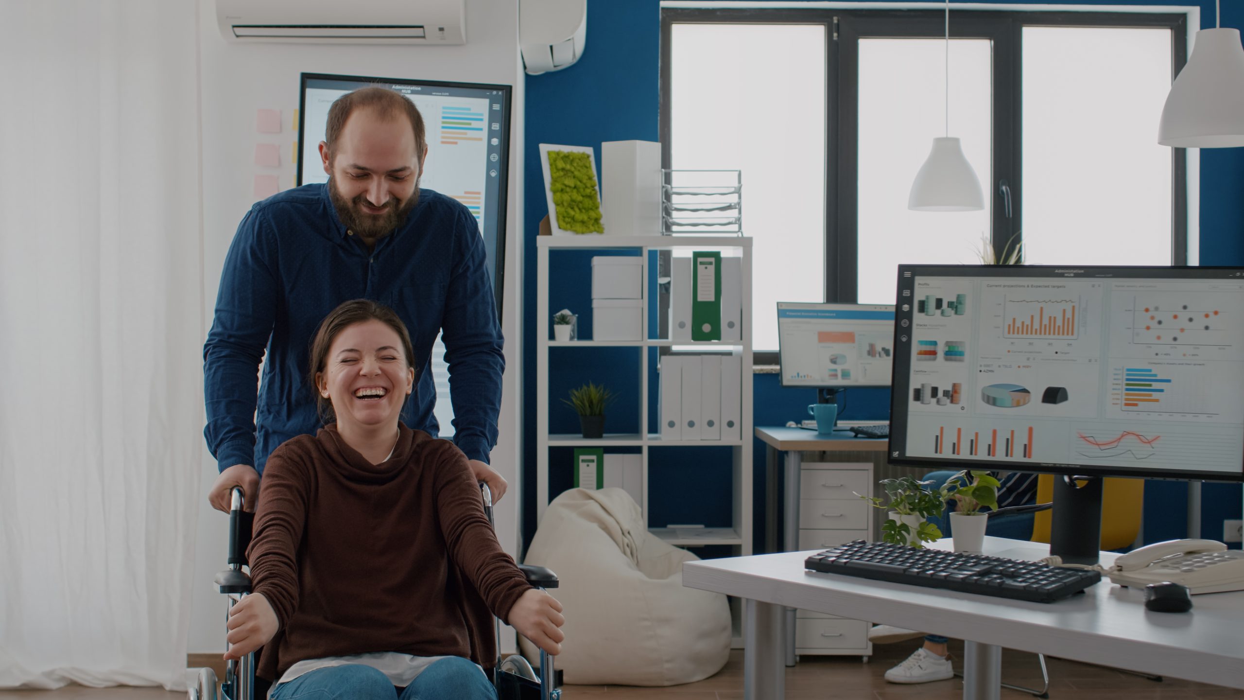 Cheerful young man pushing wheelchair with his disabled paralysed coworker